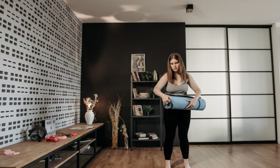 Plus size woman rolling a yoga mat in a stylish indoor setting with modern decor.